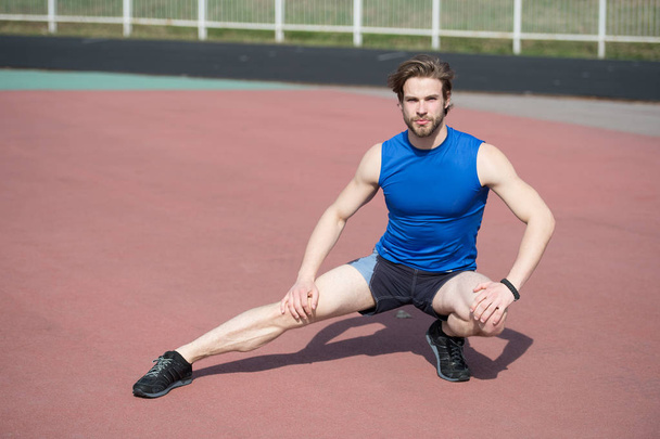 athletic bearded man with muscular body stretching on running track - 写真・画像