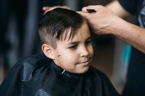menino chegando corte de cabelo por barbeiro enquanto sentado na cadeira na barbearia
. - Foto, Imagem