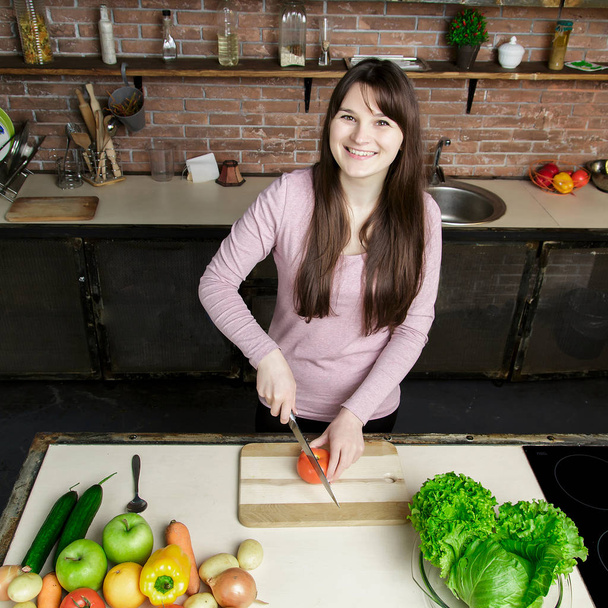 Young woman cutting vegetables using knife and cooking board. She is preparing fresh meal in the kitchen. - Photo, image