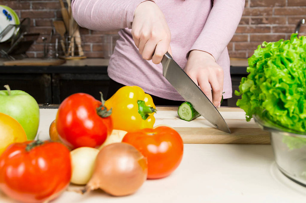 Cocinera hembra rebanando pepino verde, cocinando ensalada de verduras frescas en la tabla de cortar en su encimera de cocina
 - Foto, imagen