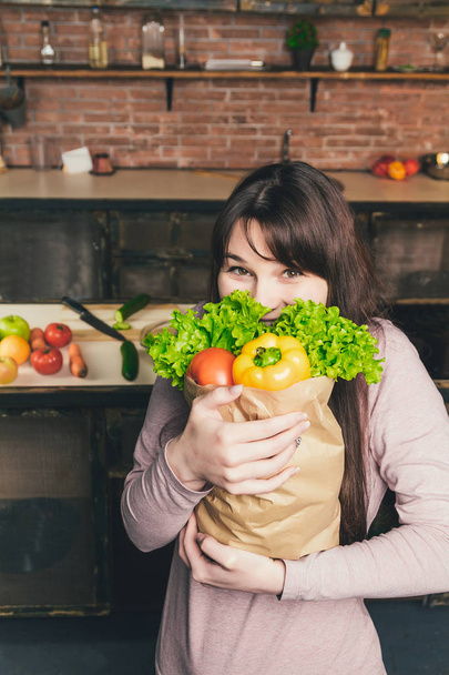 Woman holding a paper bag with fresh vegetables in the kitchen - Photo, Image