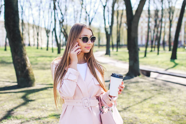 Fashionable woman with phone and cofee in the city. Fashion woman in a sunglasses and pink jacket outdoor - Φωτογραφία, εικόνα