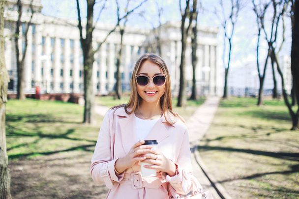 Fashionable woman with phone and cofee in the city. Fashion woman in a sunglasses and pink jacket outdoor - 写真・画像