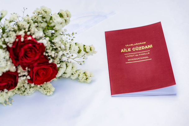 Evlilik cuzdani (avioliittolupa) valkoisella pöydällä punaisten ruusujen kanssa
 - Valokuva, kuva