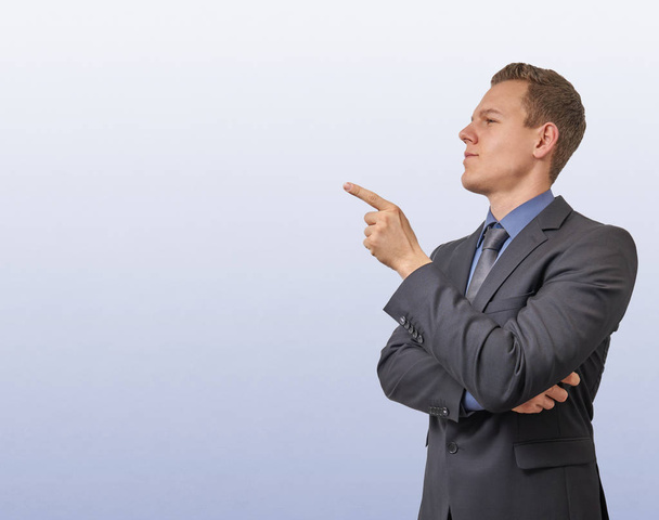 Un jeune homme d'affaires pointe son doigt sur le côté gauche - isolé avec un copyspace. Expression sceptique, critique ou analytique pour la publicité
. - Photo, image