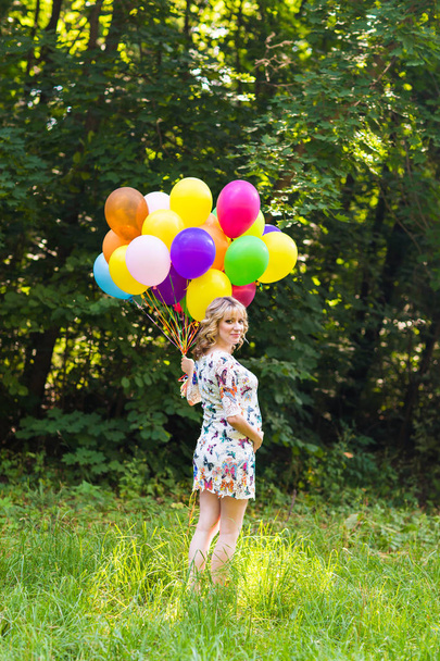 Mladá těhotná žena držící barevné balónky venku - Fotografie, Obrázek