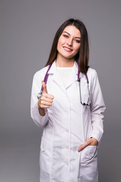 Female doctor with thumbs up gesture against grey background - Valokuva, kuva