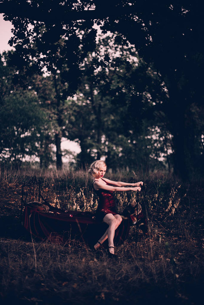 schöne und elegante blonde Frau mit roten Lippen und Haaren Wellen tragen weinroten Nachthemd posiert auf dem Bett im Freien Herbst, Retro-Vintage-Stil und Mode. - Foto, Bild