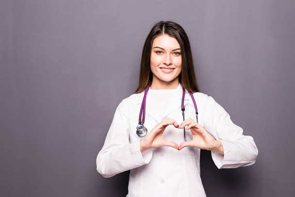 Female doctor smile and make her hand to heart shape on grey - Photo, Image