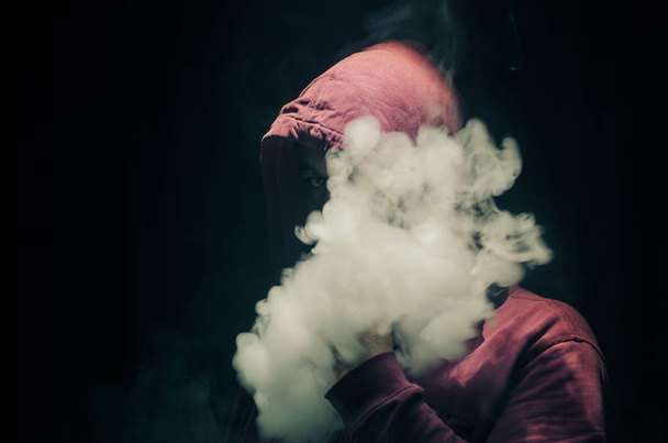 Dampfender Mann mit einem Mod. eine Dampfwolke. schwarzer Hintergrund. Verdampfen einer elektronischen Zigarette mit viel Rauch - Foto, Bild