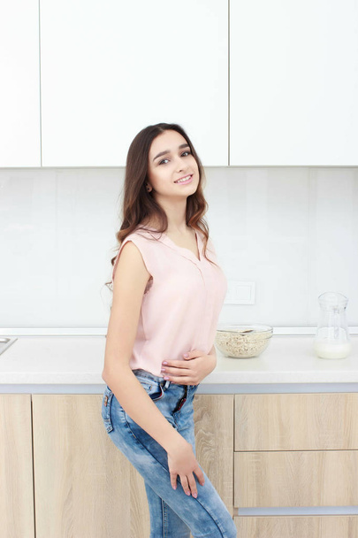 Serious attitude. Young smiling lady standing in a kitchen. - Foto, Imagen