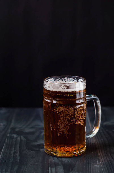 Bir bardak bira karanlık bir arka plan üzerinde. Bir bardak ahşap bir masa üzerinde hafif bira. - Fotoğraf, Görsel