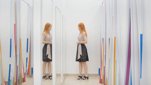 Meisje in kledingwinkel kiest jurk in de buurt van spiegel in kamer - shopping concept passen - Foto, afbeelding
