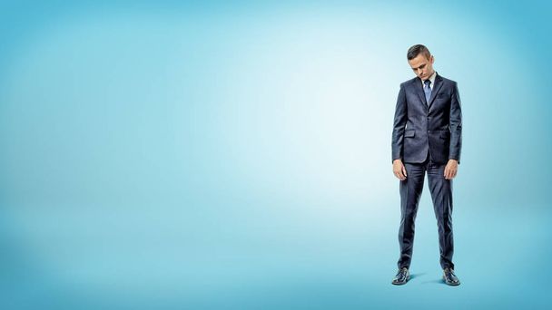 A depressed businessman standing with shoulders slumped on blue background. - Photo, Image