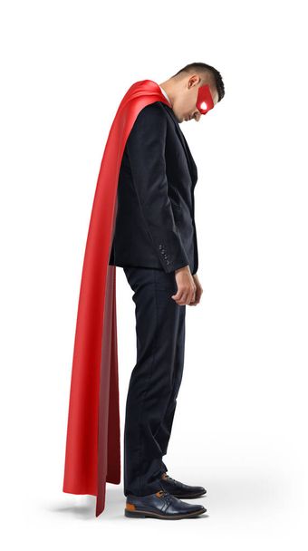 Сумний бізнесмен в супергеройському червоному мисі, що стоїть з плечима, опустився і дивиться вниз
. - Фото, зображення
