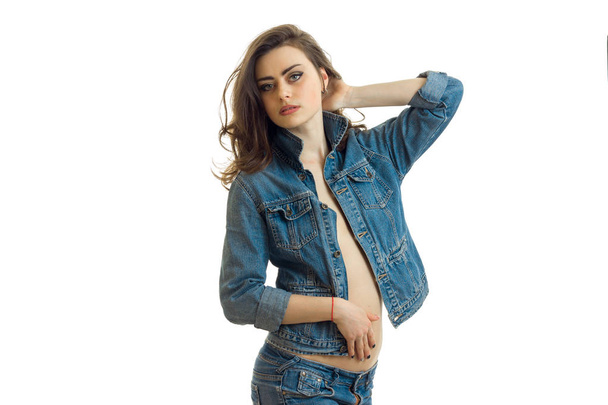 charming brunette in jeans clothes keeps the arm near the hair and looks into the distance - Фото, изображение