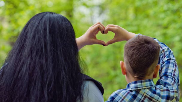 Mamma e figlio che formano un cuore con le mani su una panchina del parco
. - Foto, immagini
