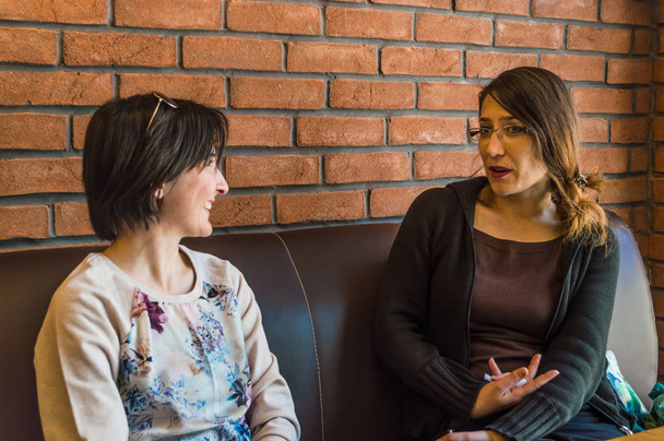 Twee brunette jonge vrouwen zitten in een cafe met gesprek - Foto, afbeelding