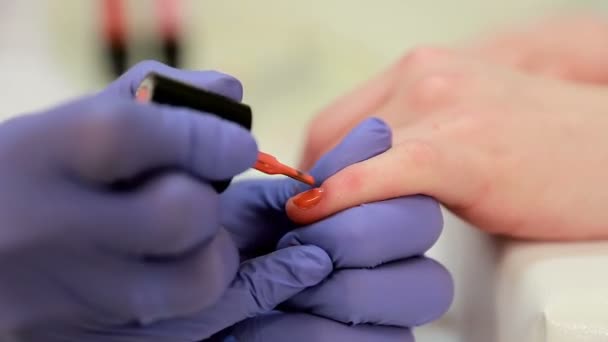 Close-up shot van een schoonheidsspecialiste nagellak op vrouwelijke nagel in een nagel salon toe te passen. Close-up van de hand van een vrouw met koraal nailpolish na de manicure. - Video