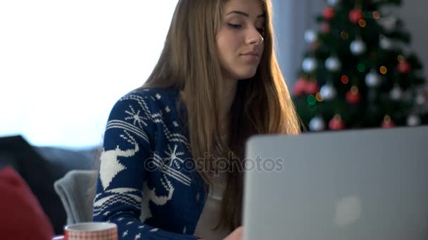 Smiling young woman typing laptop and talking on the smart phone on the christmas tree background in the living room. Close up. - Кадры, видео