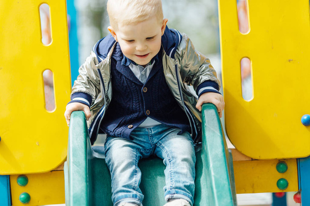 Мальчик катается на качелях на детской площадке в парке
 - Фото, изображение