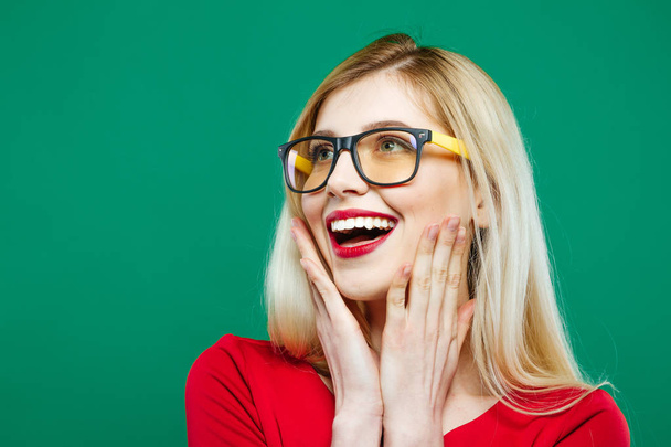 Laughing Girl in Eyeglasses and Red Top on Green Background. Closeup Portrait of Young Blonde with Long Hair and Charming Smile in Studio. - Foto, Bild