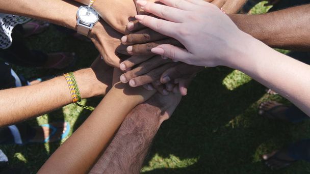 Arm of all races and colors stacked together one by one in unity and teamwork and then raised. Many multiracial hands getting together in the center of a circle and then cheer. Close up outdoor shot - Photo, Image