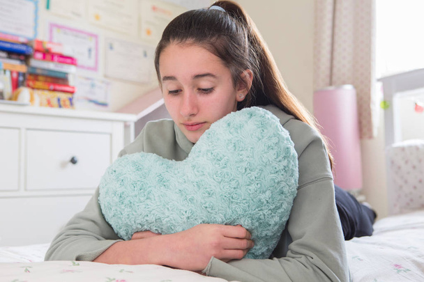 Jovem infeliz deitada na cama abraçando coração em forma de almofada
 - Foto, Imagem