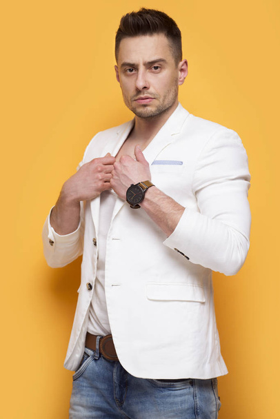 Handsome elegant man in white jacket standing on yellow background - Photo, image