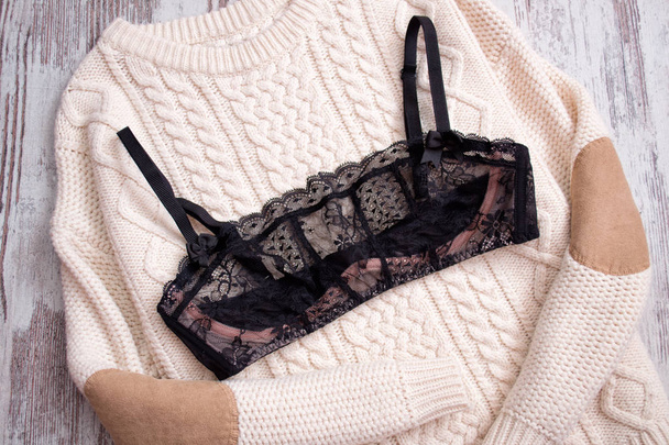 Black lace bra on a beige sweater. Fashionable concept - Photo, Image