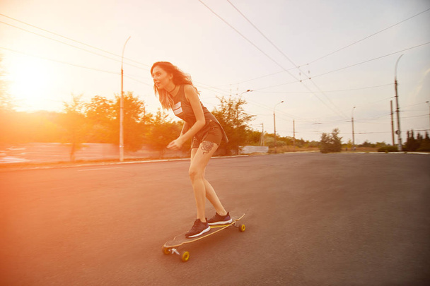 Όμορφη νεαρή κοπέλα με τατουάζ, ιππασία longboard στο ηλιόλουστο καιρό - Φωτογραφία, εικόνα