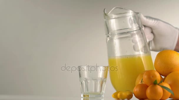The hand in white gloves is pouring the orange juice into the rocks glass placed next to the fruit composition consisted of the oranges and mandarins. - Кадры, видео