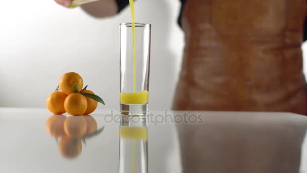 eine minimalistische Komposition des Mannes, der den Orangensaft in das hohe Glas gießt, das in der Nähe der Mandarinenpyramide steht. - Filmmaterial, Video