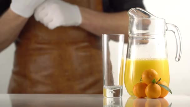 The composition of the decanter with oranged juice, high glass and mandarins at the blurred background of the cooker getting prepared. - Video, Çekim