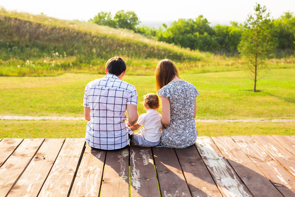 家族の肖像画。幸せな愛情のある父、母と自分の赤ちゃんの屋外の写真。パパ、ママと子に対して緑の丘。背面図. - 写真・画像