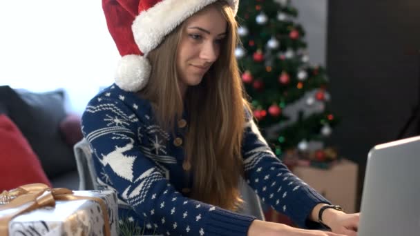 Smiling young woman chating with friend on laptop and drinking coffee on the christmas tree background in the living room. - Filmati, video