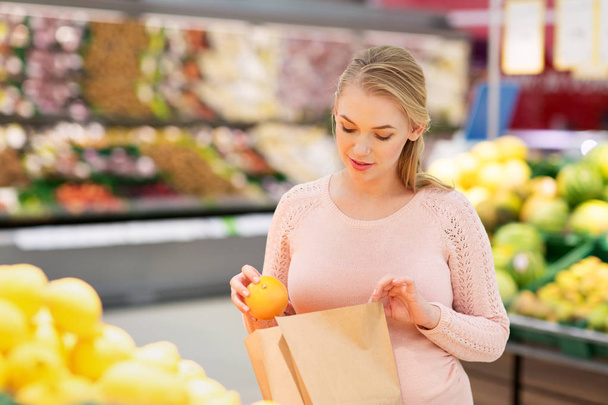 pregnant woman with bag buying oranges at grocery - Photo, Image