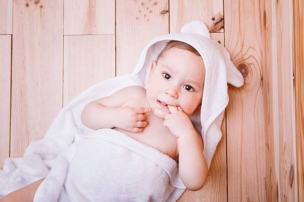 jongetje met bruine ogen is vijf maanden oud verpakt in een witte handdoek met oren op houten achtergrond . - Foto, afbeelding
