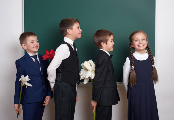 αγόρια δίνοντας κορίτσι λουλουδιών, Δημοτικό σχολείο παιδί κοντά σε ιστορικό κενό πίνακα κιμωλίας, ντυμένοι με κλασικό μαύρο κοστούμι, ομάδα μαθητών, εκπαίδευσης έννοια - Φωτογραφία, εικόνα