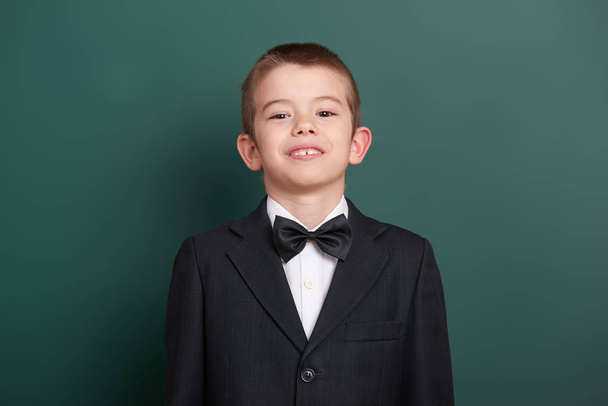 school boy portrait near green blank chalkboard background, dressed in classic black suit, one pupil, education concept - Фото, зображення