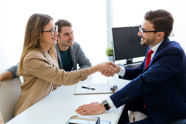 Young couple in bank office shaking hand to financial adviser. - Photo, image