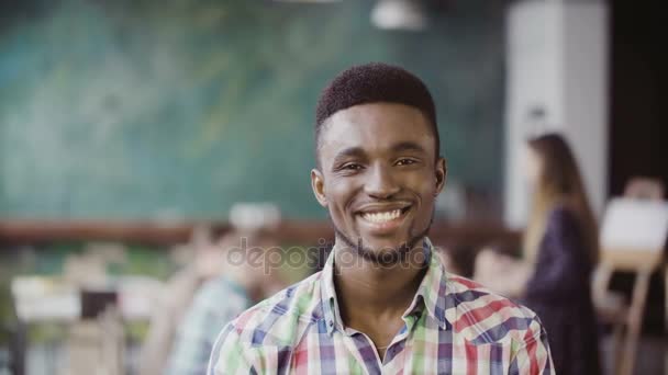Όμορφος άνδρας Αφρικής στο πολυάσχολο σύγχρονο γραφείο. Πορτρέτο του νεαρά αρσενικά επιτυχημένη βλέπουν φωτογραφική μηχανή και χαμογελαστός. - Πλάνα, βίντεο