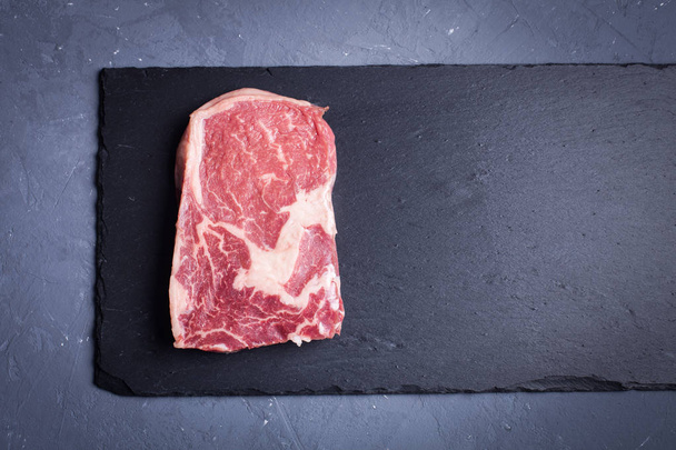 Raw marble, fresh piece of meat, black Angus ribeye steak on a dark stone background. - Photo, Image