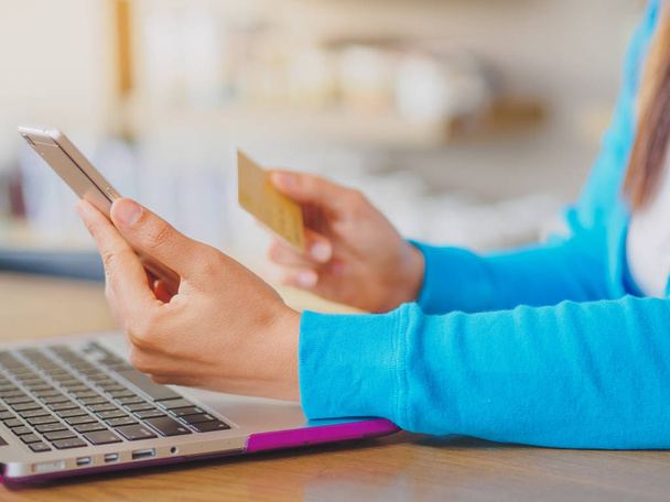 Pretty Young womans hands holding a credit card and using smartphone and laptop computer for online shopping.  - Photo, Image