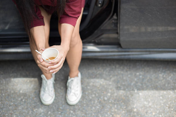 車の横に座っていると、使い捨て可能な一杯のコーヒーを保持している女性  - 写真・画像
