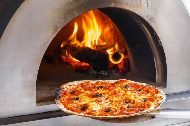 炎の背後にある薪のオーブンでピザを閉じる - 写真・画像
