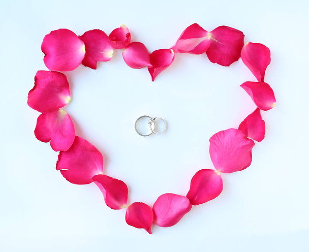 Petals of rose flower in heart shape with couple wedding rings isolated on white background. - Photo, Image