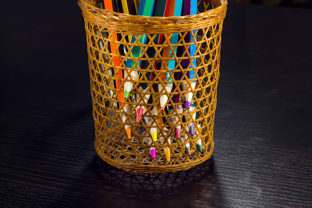 Colored pencils are visible through a wicker glass - Fotoğraf, Görsel