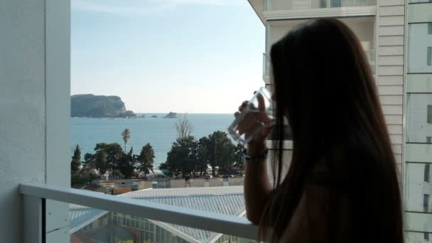 Jonge vrouw staande op het balkon en het drinken van water buiten. - Video