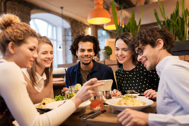 friends with smartphone eating at restaurant - Фото, зображення